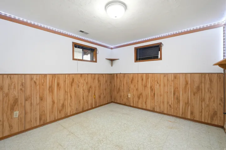 Recessed ceiling light fixture, wood-finish wall paneling, two windows with wood-trim framing, and a corner shelf