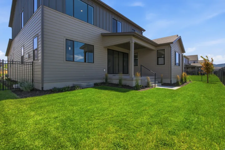 Expansive green lawn with a black metal fence, covered patio, and multi-story exterior architecture featuring paneling and siding