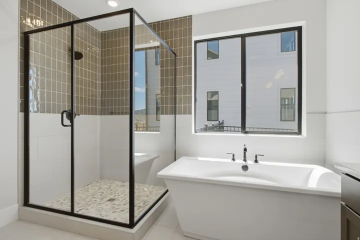 Glass-enclosed shower with pebble-tile floor and bench, freestanding soaking tub with contemporary fixtures, and large window