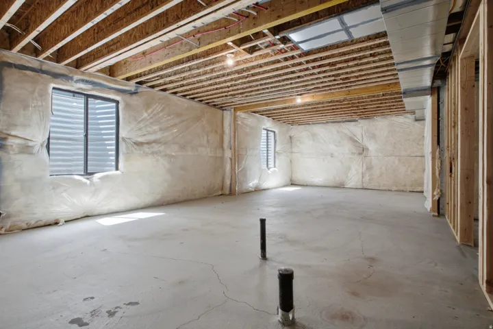 Expansive unfinished space featuring exposed ceiling joists, concrete flooring, and multiple windows