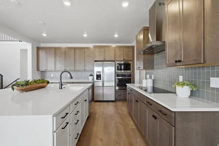 Kitchen featuring an expansive island with a built-in sink, stainless steel appliances, a tile backsplash, and recessed lighting