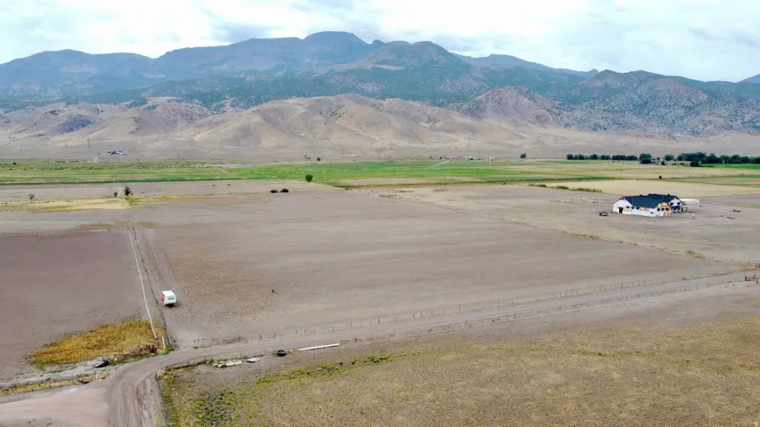 Expansive land featuring a single-story residence with a dark roof and mountain scenery