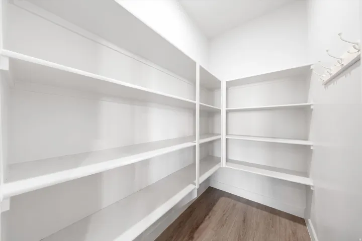 Expansive pantry featuring built-in white shelving, integrated coat hooks, and wood-finish flooring