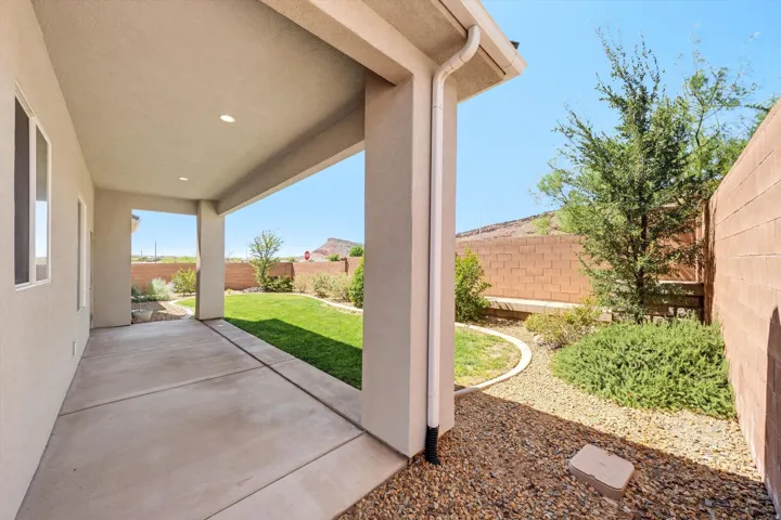 Covered patio with concrete flooring and structural columns opening to a manicured lawn, mature landscaping, and desert mountain backdrop