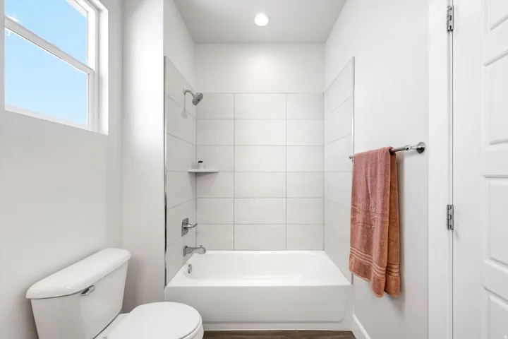 White tile shower surround with a built-in shelf, chrome shower fixtures, and a white porcelain bathtub