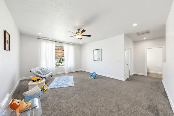 Spacious carpeted room featuring a ceiling fan, recessed lighting, and a large window with sheer white curtains