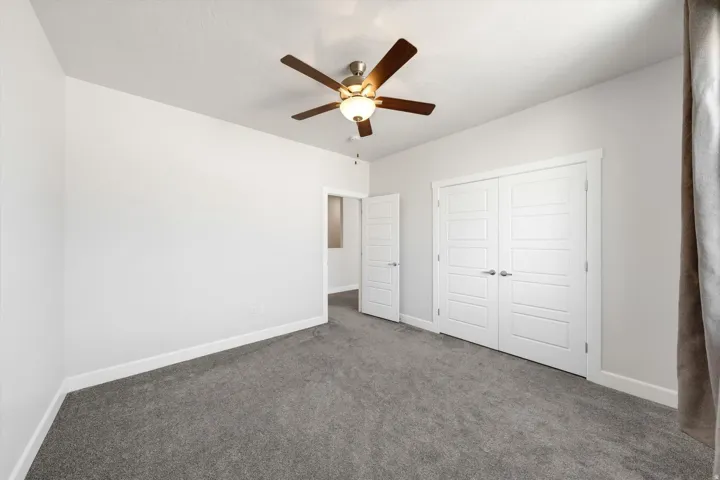 Spacious bedroom with neutral wall finishes, plush carpeting throughout, ceiling fan with integrated lighting, and dual closet doors providing ample storage