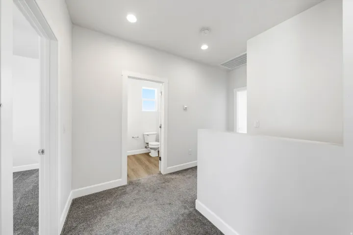 Recessed lighting, light gray wall finishes, gray carpet flooring, white trim, and wood-finish flooring in the bathroom