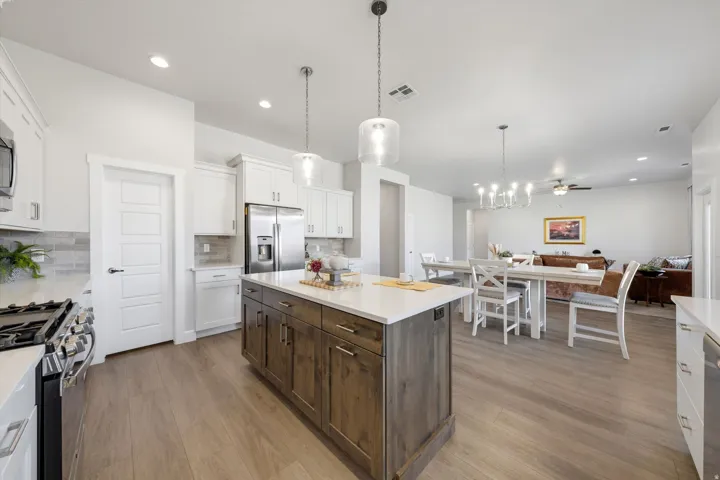 Kitchen featuring a wood-finish island with a light-toned countertop, pendant lighting, stainless steel appliances, and wood-finish flooring