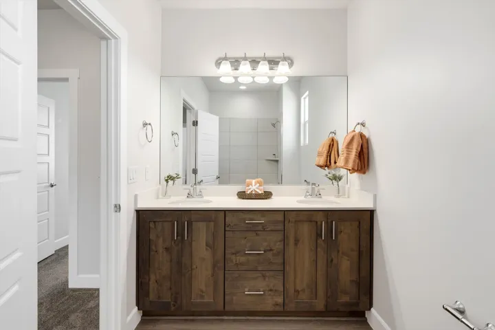 Dual sink vanity with wood-finish cabinetry, white countertop, and brushed nickel hardware