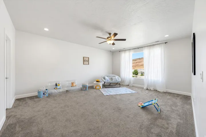 Spacious room featuring neutral carpet flooring, recessed lighting, ceiling fan, and a large window with sheer drapery