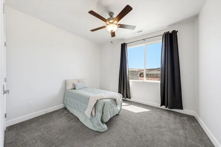 Recessed window with dark curtain rods, ceiling fan with light fixture, light gray carpet, and white walls