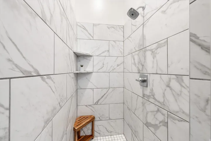 Shower enclosure with large format white and gray veined wall tiles, built-in shower niche, chrome showerhead, and coordinating chrome fixtures