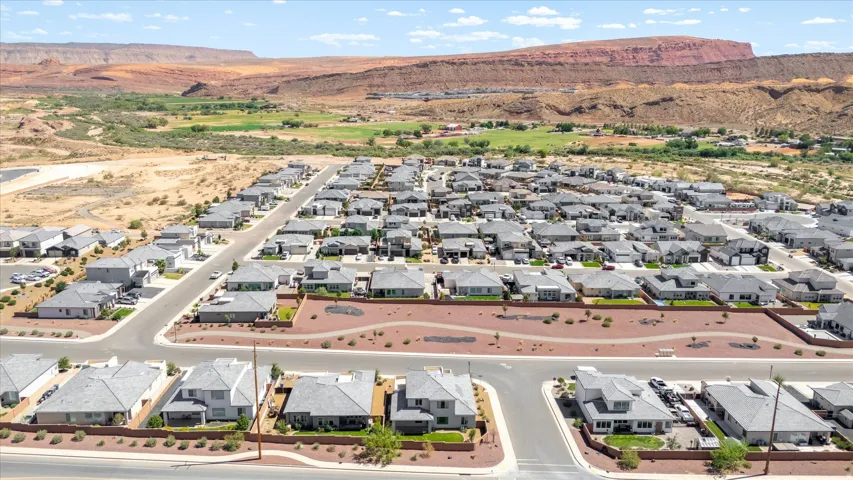 Expansive residential development featuring uniform grey-toned roofs, concrete streets, and a desert landscape backdrop with red rock formations