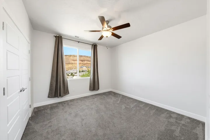 Bright secondary bedroom featuring neutral carpeting, ceiling fan with integrated lighting, and large window with custom drapery framing expansive territorial views