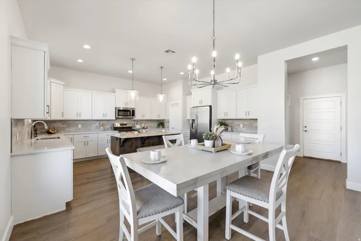White shaker cabinetry, stainless steel appliances, wood-finish flooring, recessed lighting, and a large central island with seating
