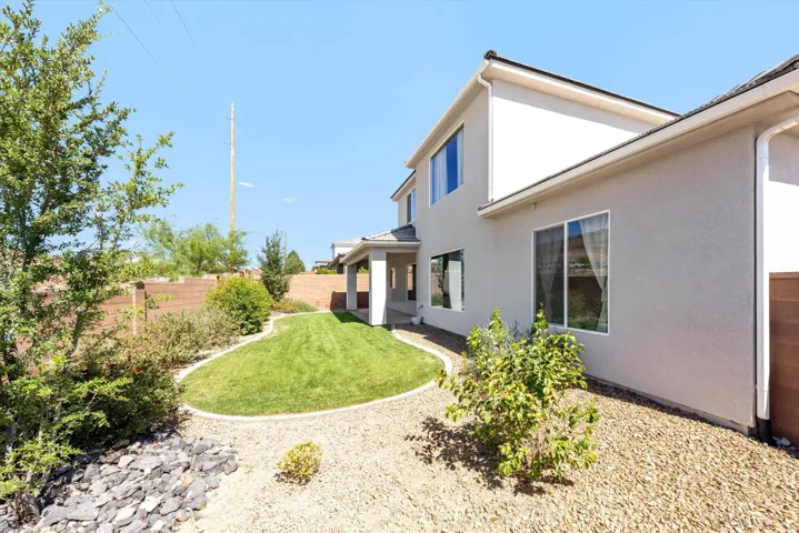 Exterior stucco finish, multiple windows, covered patio, manicured lawn, and low-maintenance landscaping