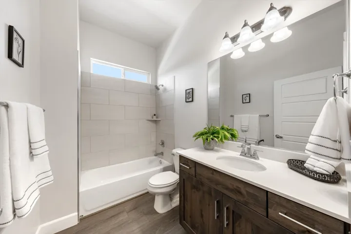 Bathroom featuring a wood-finish vanity with an integrated sink, a large mirror, a four-light fixture, and wood-finish flooring