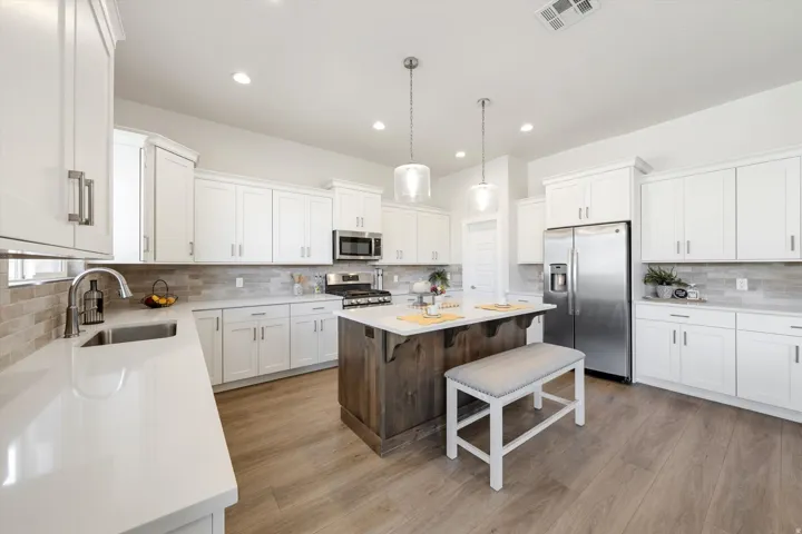 White shaker cabinetry, light-toned countertops, stainless steel appliances, wood-finish flooring, and a kitchen island with pendant lighting