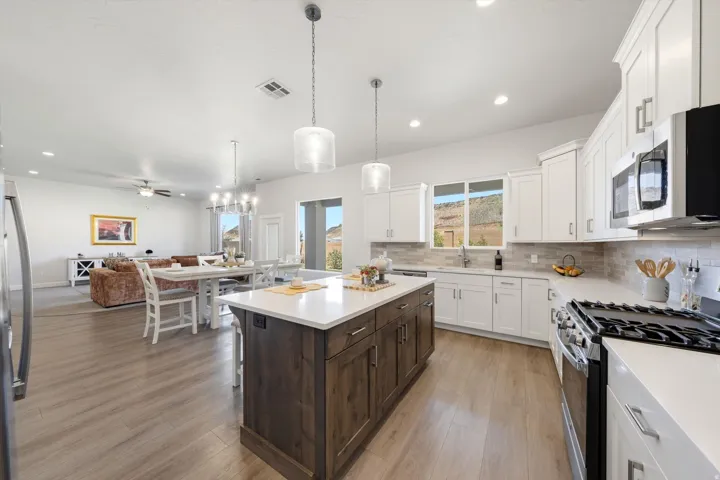 Open-concept living area featuring wood-finish flooring, a kitchen island with a light-toned countertop, white cabinetry with stainless steel appliances, and recessed lighting