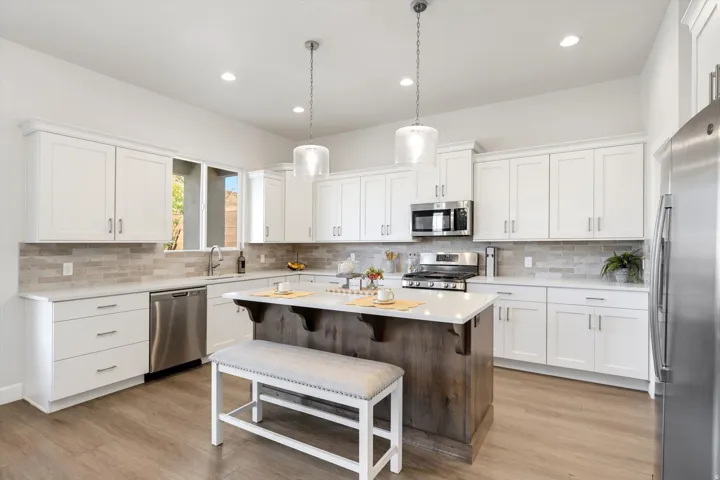 Kitchen featuring white cabinetry, stainless steel appliances, a center island with a wood-finish base, pendant lighting, and wood-finish flooring