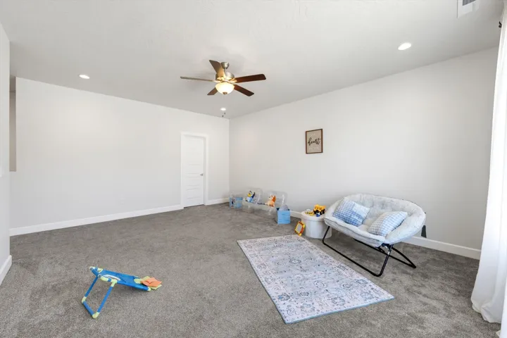 Expansive room with neutral carpet flooring, recessed lighting, white walls, a ceiling fan, and a solid white door