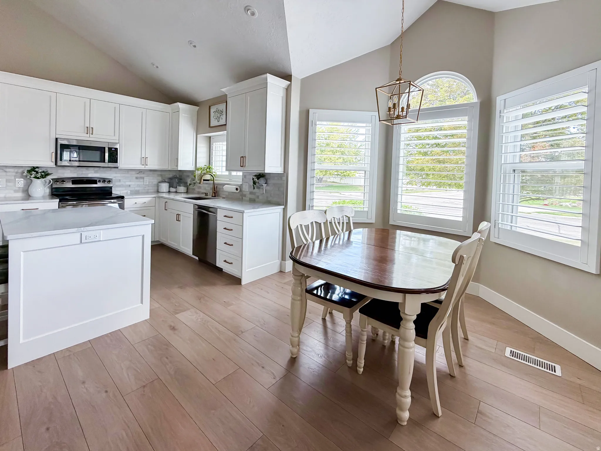 Vaulted ceiling kitchen with white cabinetry, stainless steel appliances, stone countertops, and wood-finish flooring