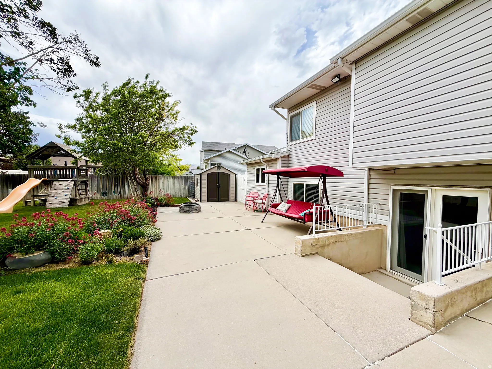 Spacious concrete patio with direct access to lower level, perimeter landscaping, and a separate storage shed