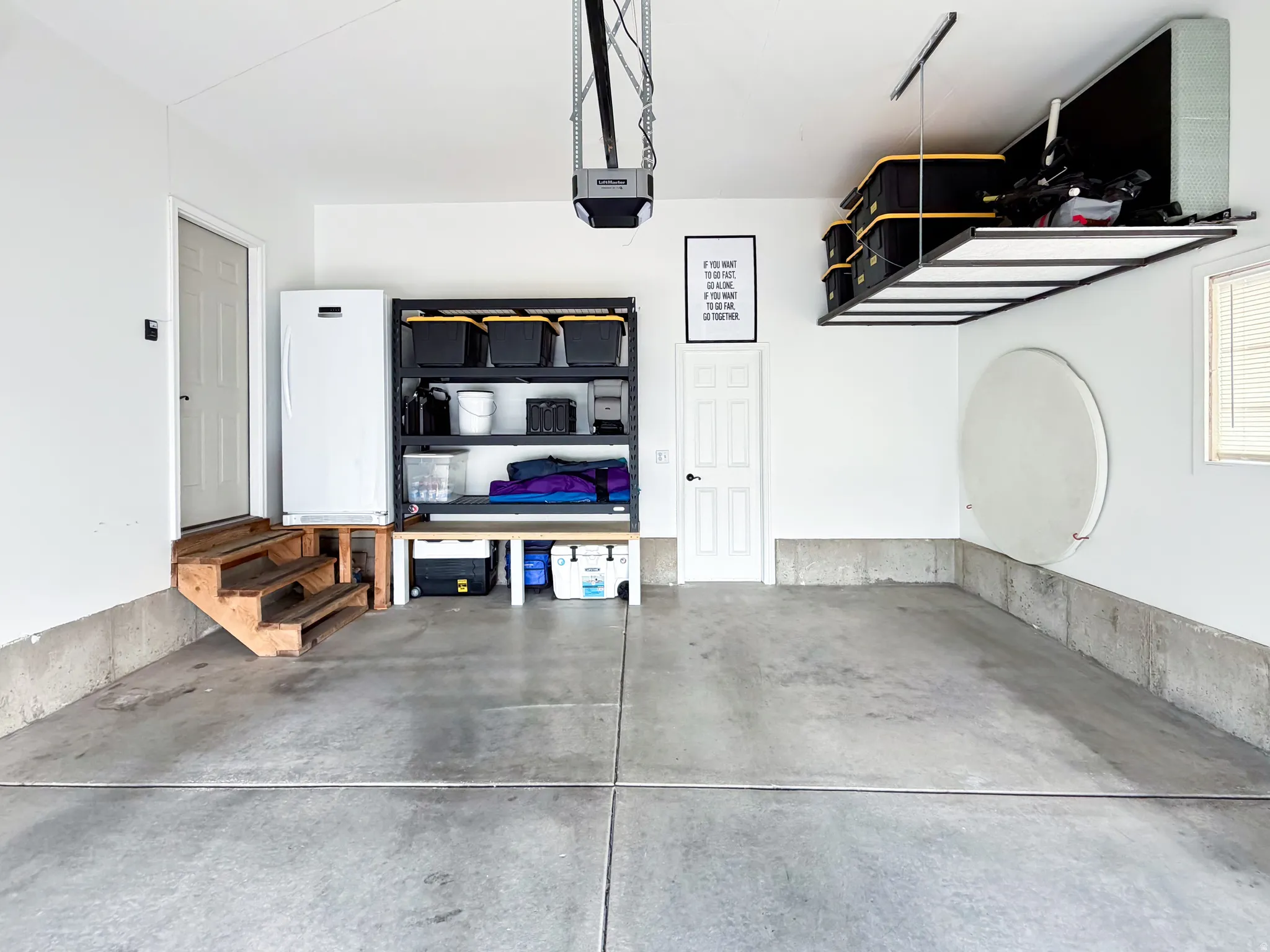 Concrete flooring with built-in overhead storage racks, an automatic garage door opener, and a side access door