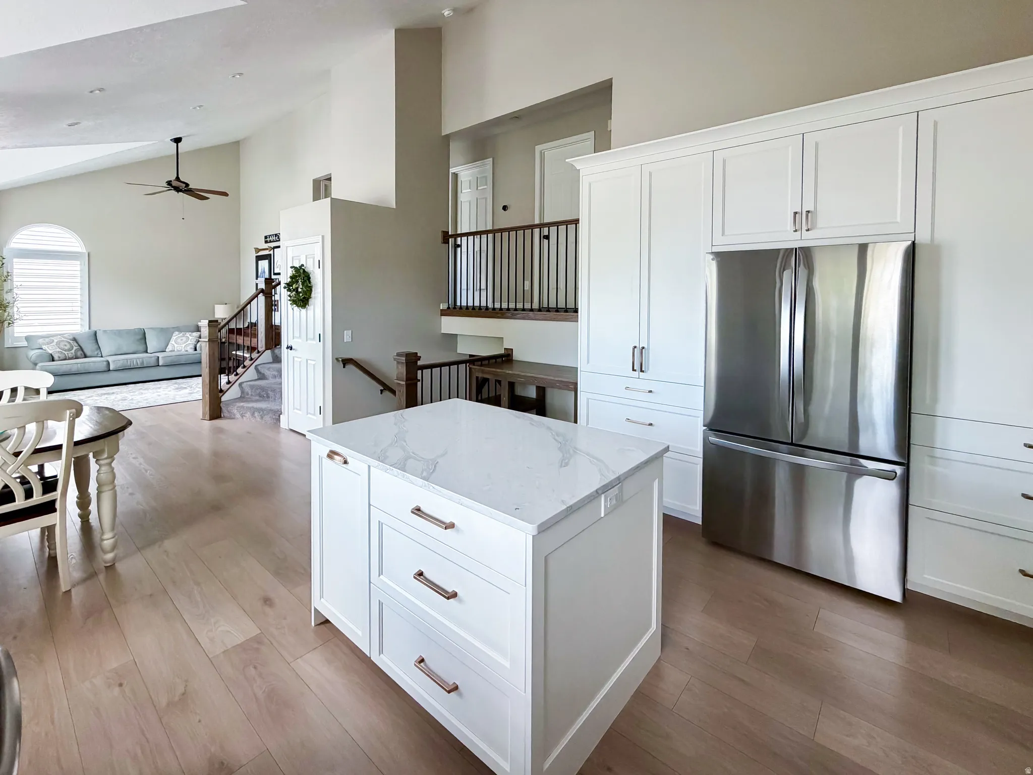 Kitchen island with a light-toned countertop, white cabinetry with bronze hardware, stainless steel French door refrigerator, and wood-finish flooring