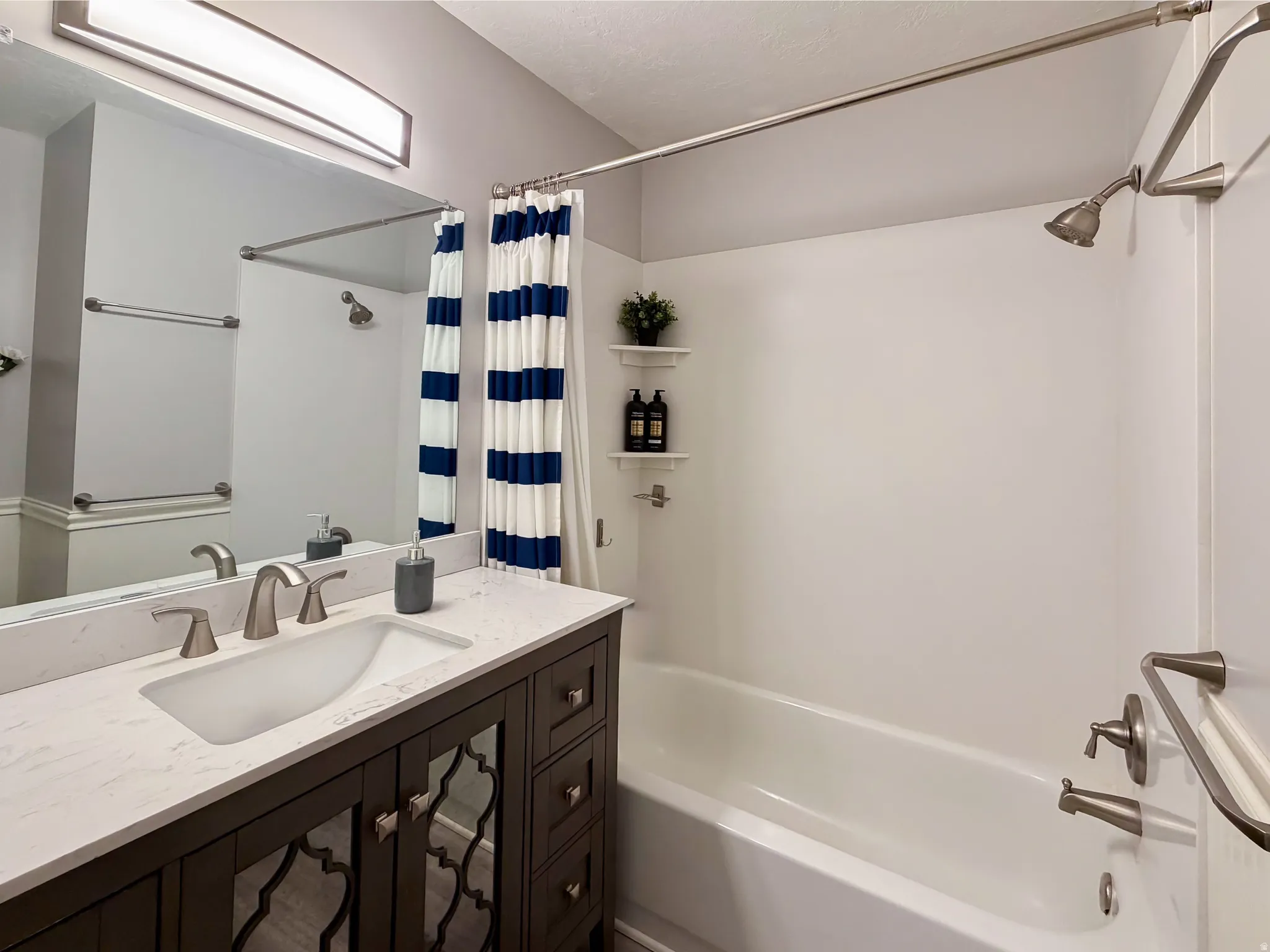 Bathroom featuring a vanity with an integrated sink, brushed nickel fixtures, a tub with a shower, and wall-mounted shelving