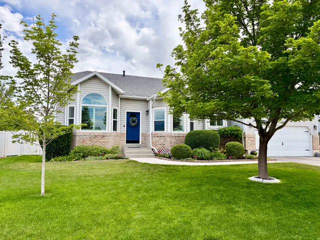 Gray siding exterior with brick accents, prominent arched window, attached garage, and mature landscaping