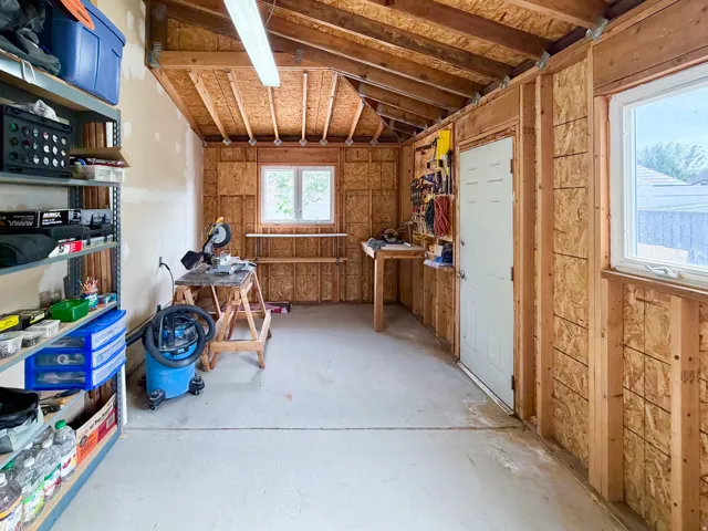 Utility space featuring exposed wood framing, concrete flooring, dual windows, and built-in shelving