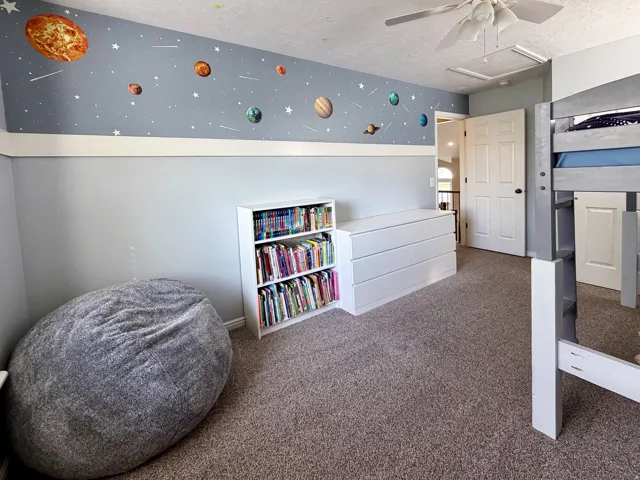 Plush carpet flooring, ceiling fan, built-in shelving, and a wall decal accent