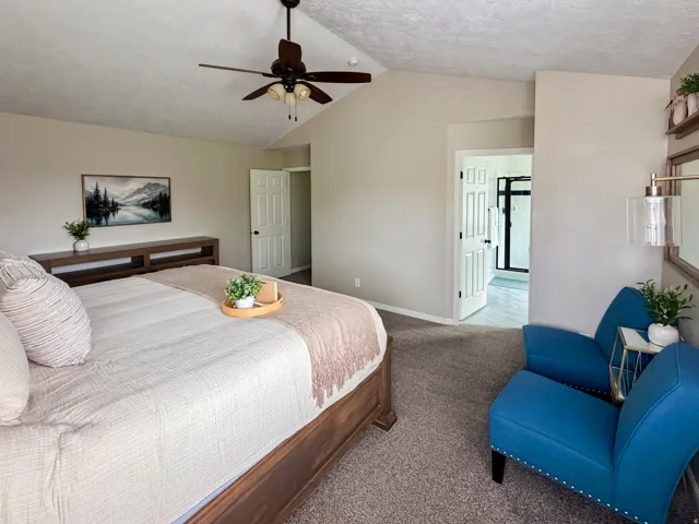 Vaulted ceiling with a ceiling fan, carpeted flooring, and an en-suite bathroom with a glass-enclosed shower