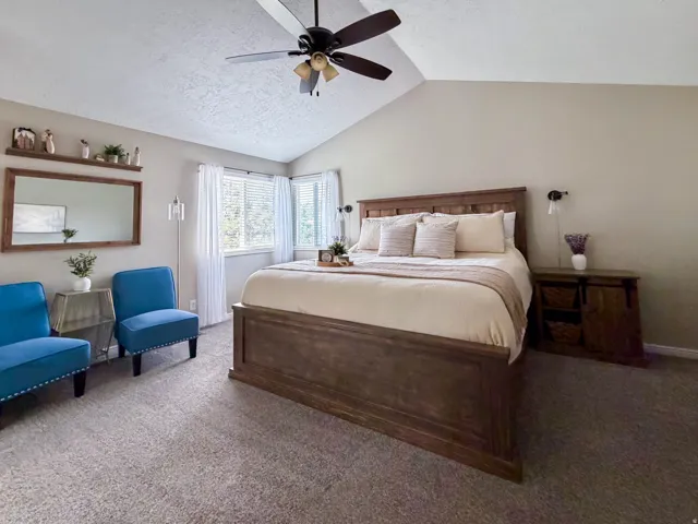 Vaulted ceiling with a ceiling fan, carpeted flooring, corner window configuration, and a built-in wall shelf with mirror