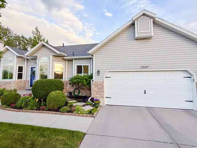 Light-toned siding exterior featuring a multi-pane garage door, a decorative gable vent, brick detailing, and a landscaped garden bed with a stone border