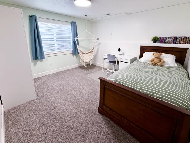 Plush carpeting, a large window with blinds, a built-in wall shelf, and a ceiling-mounted light fixture