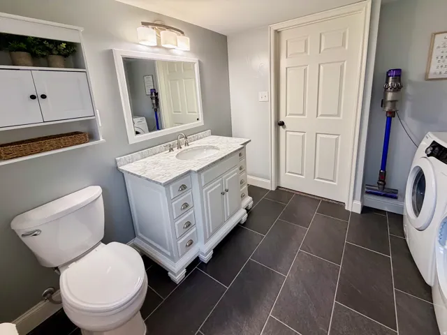 White vanity with an integrated sink and stone countertop, complemented by a framed mirror and wall-mounted light fixture