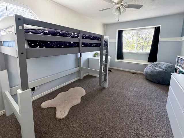 Built-in window seat, ceiling fan, carpeted flooring, and a dedicated desk space under the lofted bed frame