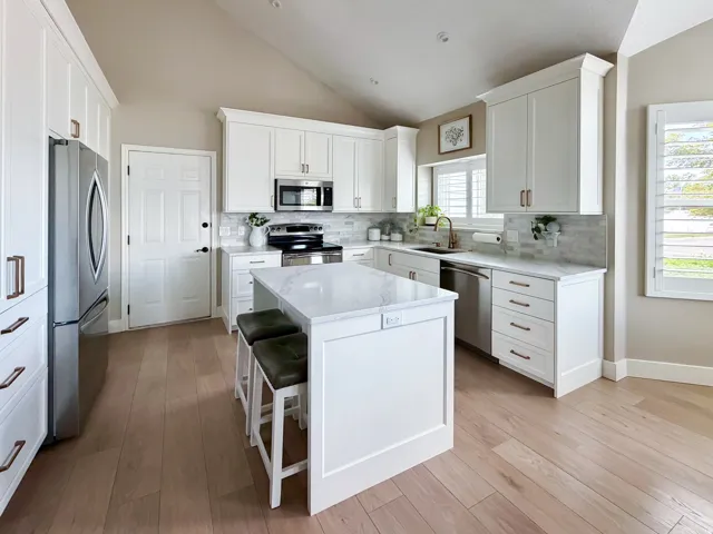 Vaulted ceiling kitchen featuring white cabinetry, a large center island with countertop seating, stainless steel appliances, and wood-finish flooring