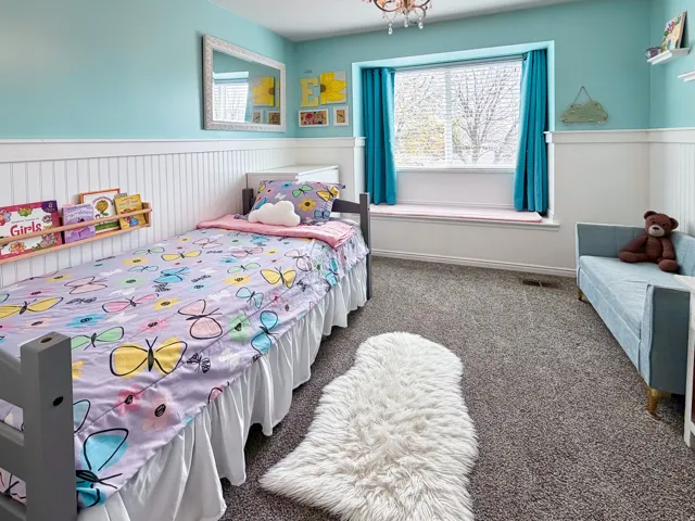 Window with cushioned sill, wall-mounted shelving, wainscoting, and broadloom carpet