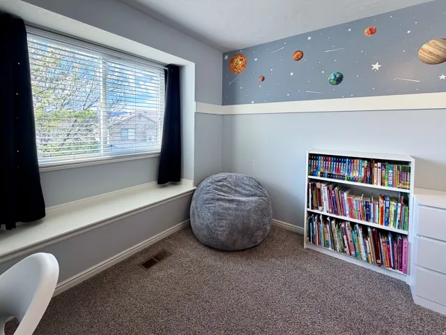 Window with white blinds and black drapes, built-in window bench, carpeted flooring, two-tone painted walls, and a built-in white bookshelf