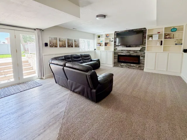 Recessed lighting, built-in shelving, stone-faced fireplace with mantel, French doors, and mixed flooring