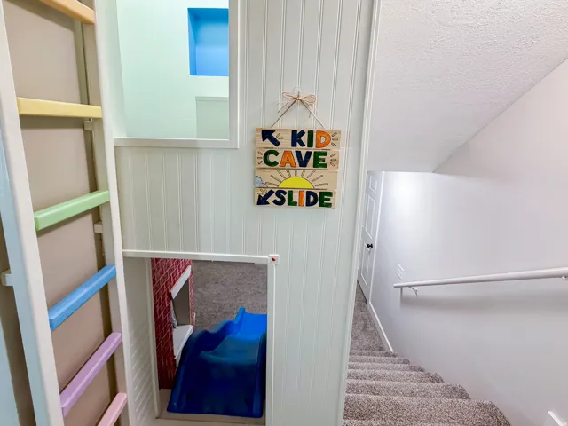 Carpeted staircase with white handrail, beadboard paneling, and a built-in play feature with a ladder and slide
