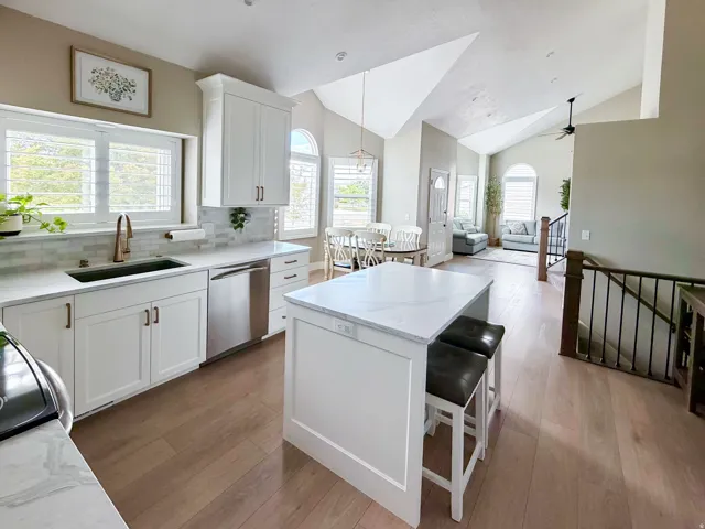 Vaulted ceilings, wood-finish flooring, white shaker cabinetry, stainless steel appliances, and a kitchen island with stone countertops