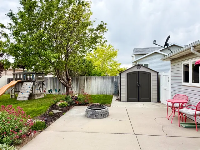 Expansive concrete patio with a stone-finish fire pit, mature tree, and privacy fencing