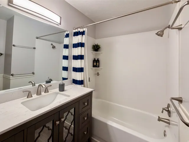 Bathroom featuring a vanity with an integrated sink, brushed nickel fixtures, a tub with a shower, and wall-mounted shelving