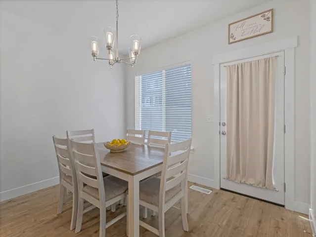 Recessed window with blinds, wood-finish flooring, white walls, and a modern chandelier