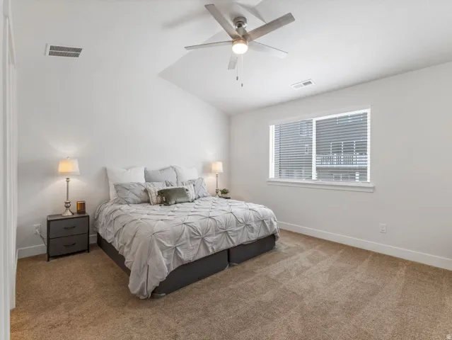 Vaulted ceiling with a ceiling fan, neutral carpeting, and a window with blinds